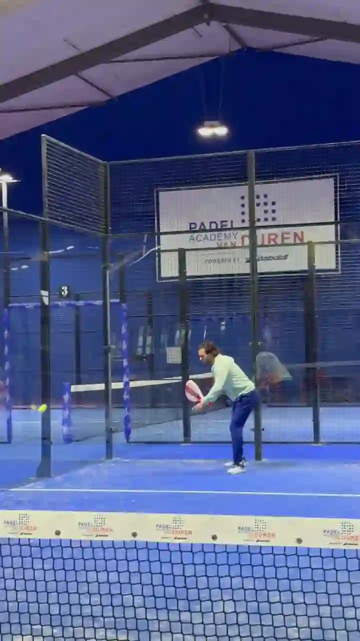 Bennet van Duren slaat ballen op een van de indoor banen, met het bord Padel Academy van Duren op de achtergrond